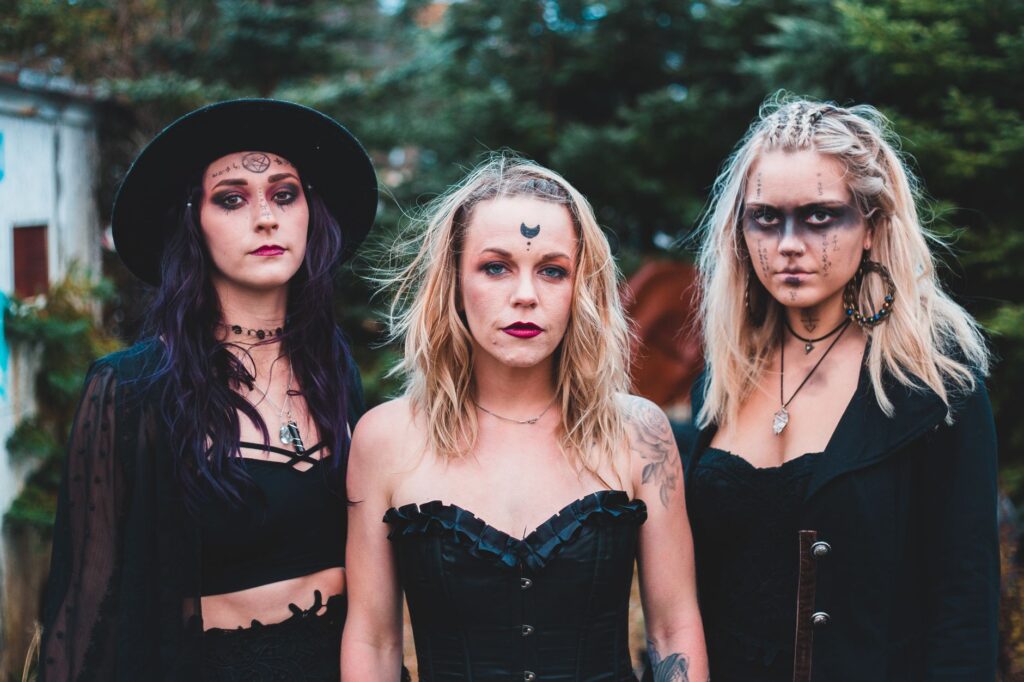 Group of females wearing black clothes with boho accessories and makeup looking at camera in nature