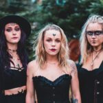 Group of females wearing black clothes with boho accessories and makeup looking at camera in nature