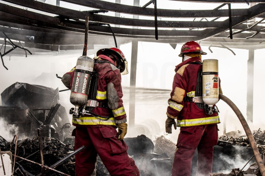 Firefighters in protective gear extinguishing flames in a charred structure.