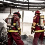 Firefighters in protective gear extinguishing flames in a charred structure.