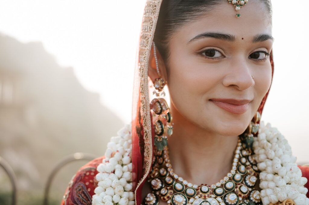 Beautiful Indian bride adorned with traditional jewelry and floral garland, smiling softly against a soft blurred background.