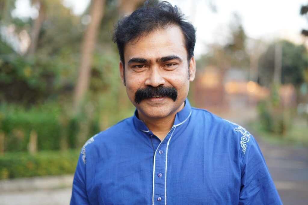 Portrait of a happy man with mustache smiling outdoors in a blue shirt.