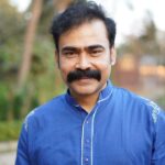 Portrait of a happy man with mustache smiling outdoors in a blue shirt.