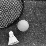 From above of black and white tennis racket with ball and shuttlecock placed on asphalt ground