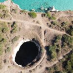 Drone shot of a coastal landscape with a prominent sinkhole and turquoise sea.