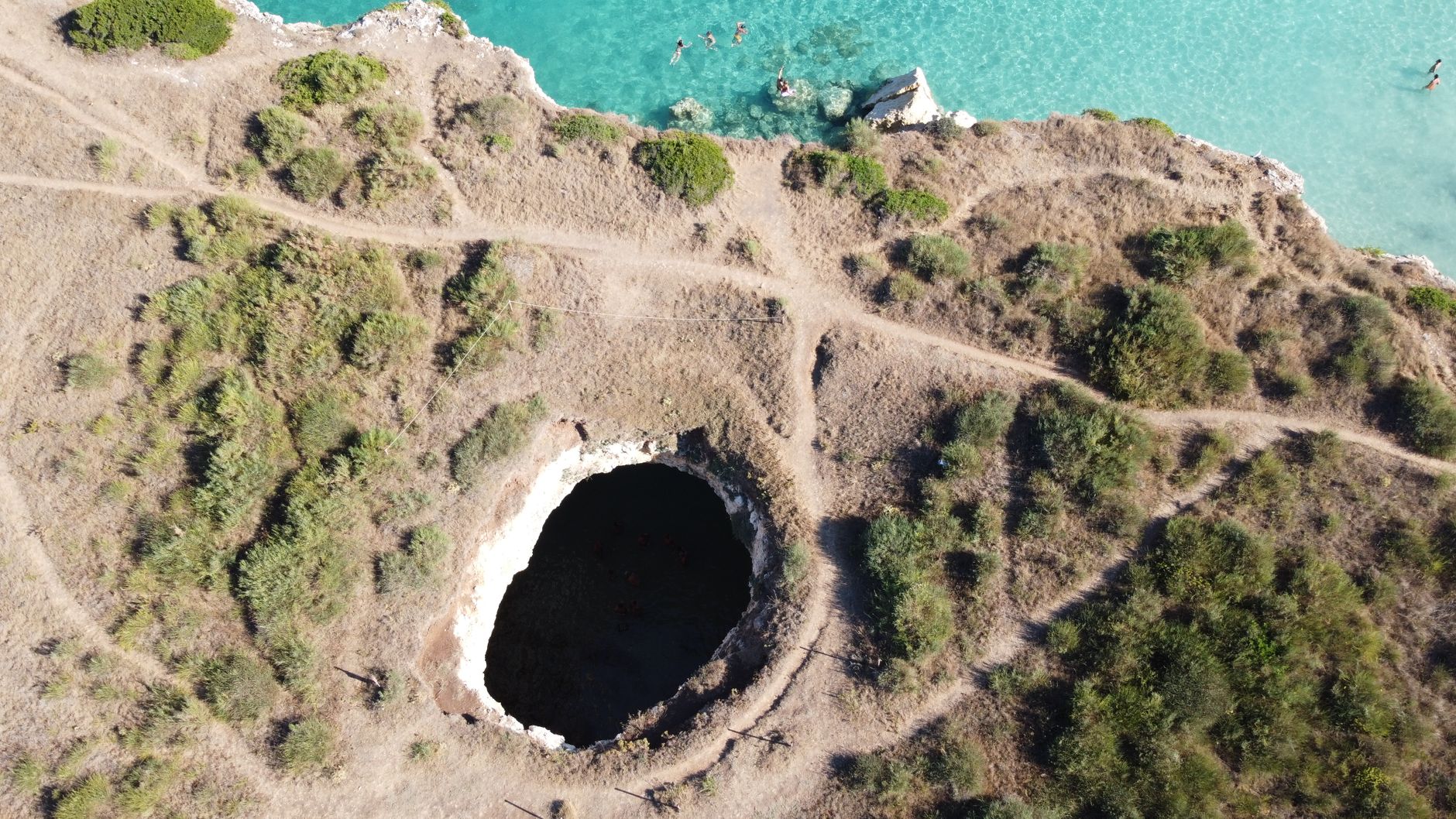 Drone shot of a coastal landscape with a prominent sinkhole and turquoise sea.