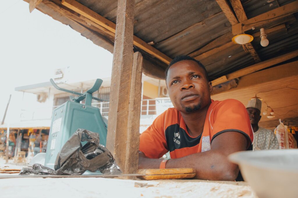 A thoughtful moment of an African man sitting at a market stall with a mechanical scale, surrounded by rustic elements.