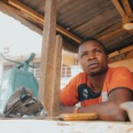 A thoughtful moment of an African man sitting at a market stall with a mechanical scale, surrounded by rustic elements.