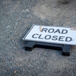 A road closed sign lies on a gravel pathway, indicating a blocked road ahead.