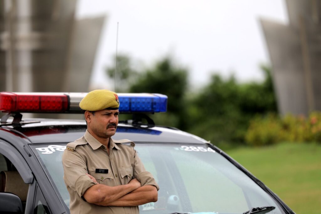 Indian police officer with arms crossed standing by a patrol car outdoors, showcasing authority and law enforcement presence.