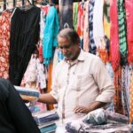 A lively street market in Bengaluru with vibrant fabrics and interactions between vendors and customers.