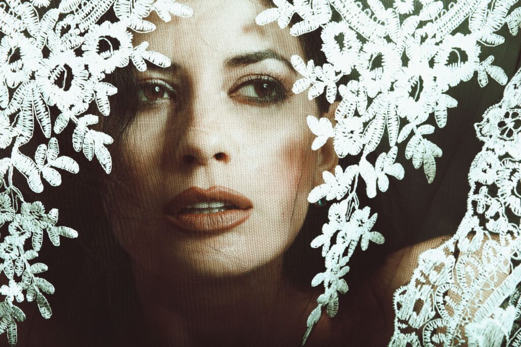 Artistic portrait of a stylish woman peering through a delicate lace veil.
