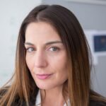 Close-up portrait of a confident woman with long hair indoors, expressing warmth and professionalism.