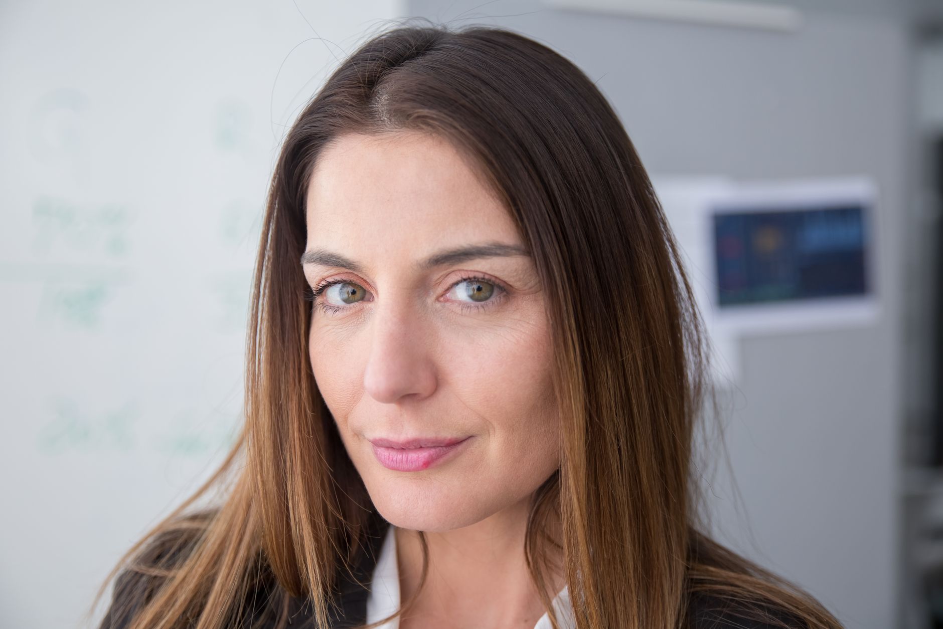 Close-up portrait of a confident woman with long hair indoors, expressing warmth and professionalism.