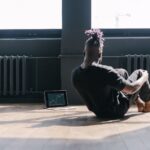Man doing sit-ups near a laptop showing stock market trends in a bright room.