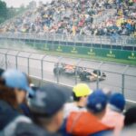 High-speed Formula One car racing on a wet track with a packed crowd of spectators.