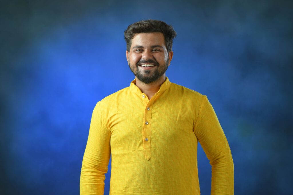 Cheerful man wearing traditional yellow kurta posing against a vibrant blue background.