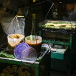 A vibrant street food scene at night featuring a vendor grilling ketan rice cakes in Indonesia.