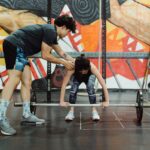 A coach instructs a young woman in proper barbell lifting technique at the gym.