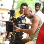 Filmmaker using a professional video camera on an outdoor set, surrounded by crew members.