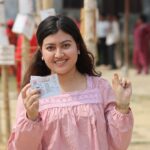 Young woman proudly displays voting ticket at outdoor polling station in Nepal.