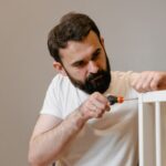 A man focusing closely on assembling a baby crib with a screwdriver in a well-lit room.