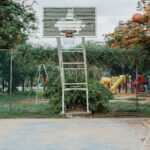 An African American man shoots a basketball in an outdoor court surrounded by lush greenery.
