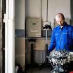 A mechanic in blue coveralls inspects an engine in a repair shop.