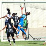 Goalkeeper leaps to make a save during an intense women's soccer match.