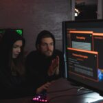 Cybersecurity experts in hoodies analyzing encrypted data on computer screens in an indoor setting.