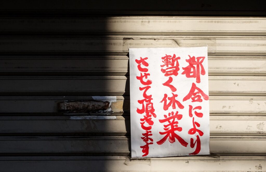 A handwritten Japanese closure sign on a metal storefront shutter, partially shadowed.