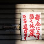 A handwritten Japanese closure sign on a metal storefront shutter, partially shadowed.