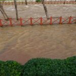 A city park flooded by a swollen river after heavy rainfall, showing the impact of severe weather.