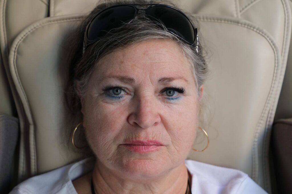 Portrait of a senior woman with sunglasses and hoop earrings, seated indoors, expressing calm.