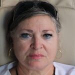Portrait of a senior woman with sunglasses and hoop earrings, seated indoors, expressing calm.