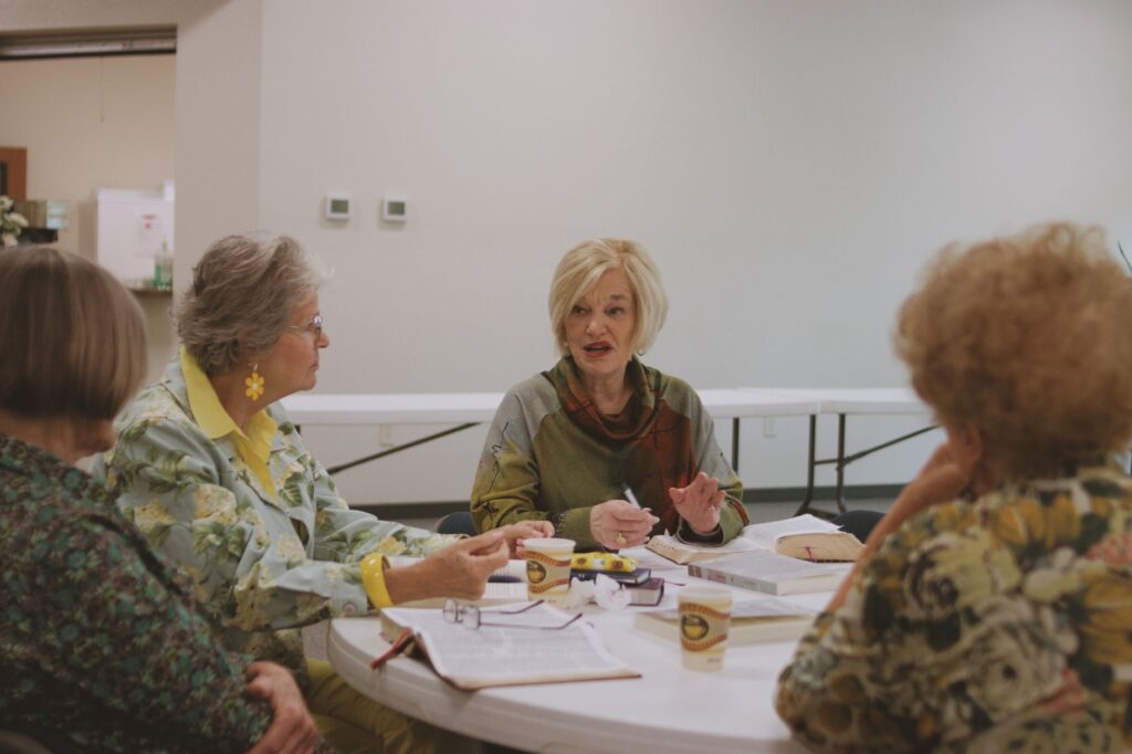 An intergenerational group of women engaged in a Bible study session indoors.