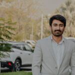 A man in a light suit standing outdoors in Islamabad, Pakistan, exuding confidence.