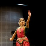 A Bharatanatyam dancer in traditional attire gracefully performing a classical Indian dance on stage.