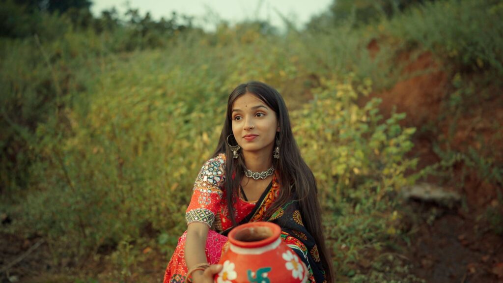 A young woman in colorful traditional Indian clothing with a painted clay pot outdoors.