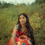 A young woman in colorful traditional Indian clothing with a painted clay pot outdoors.