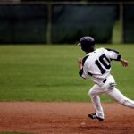 A young baseball player in uniform sprints towards base on a sunny day.