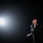 A passionate female singer performs on stage under a dramatic spotlight.