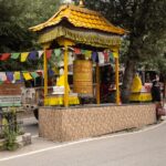 Large Buddhist prayer wheel with colorful flags in a peaceful outdoor setting, capturing local culture and spirituality.