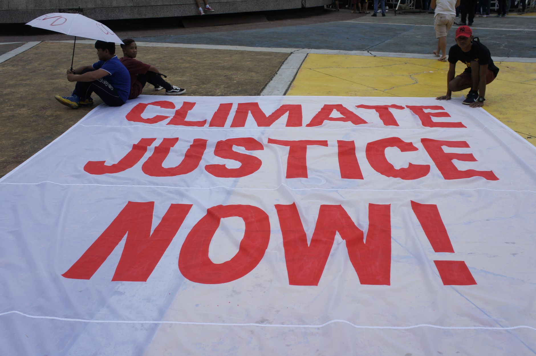 Large protest banner reading 'Climate Justice Now!' displayed outdoors during a demonstration.