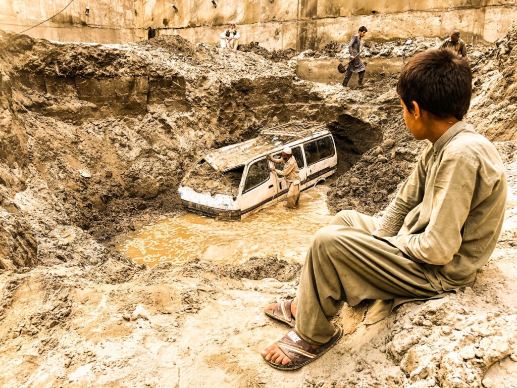 A child watches as a van is trapped in flood debris in Madyan, Pakistan, highlighting the aftermath of natural disaster.
