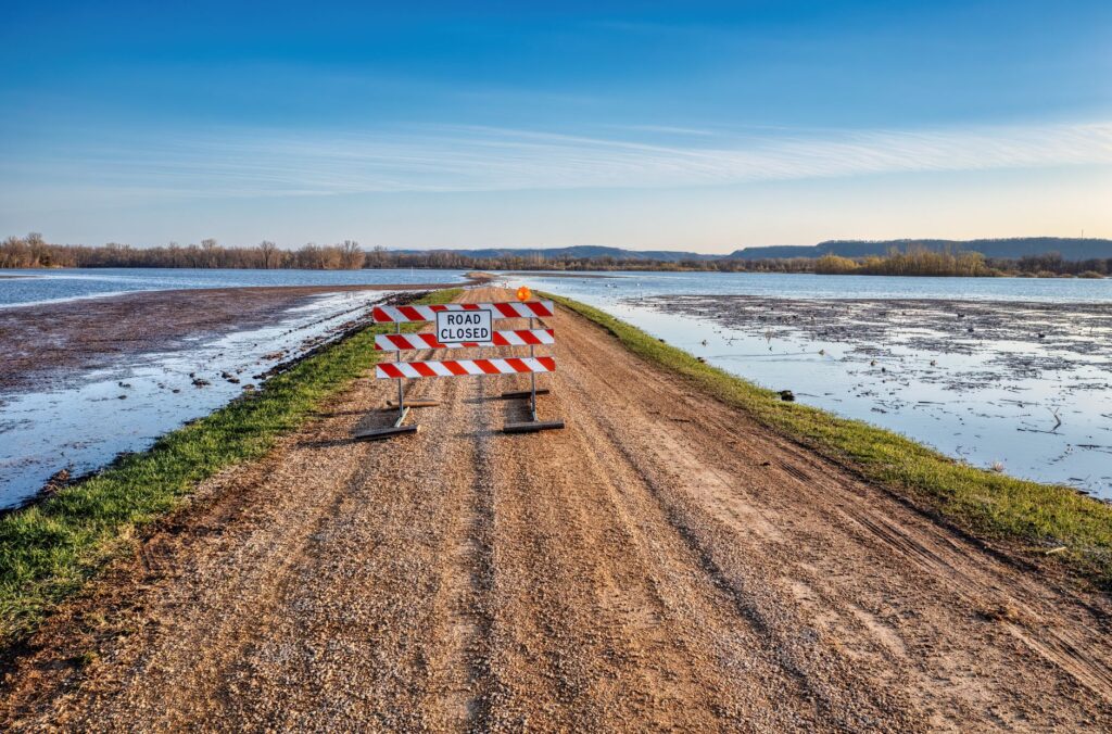 A road closed sign on a gravel path next to a flooded area in Kellogg, MN.