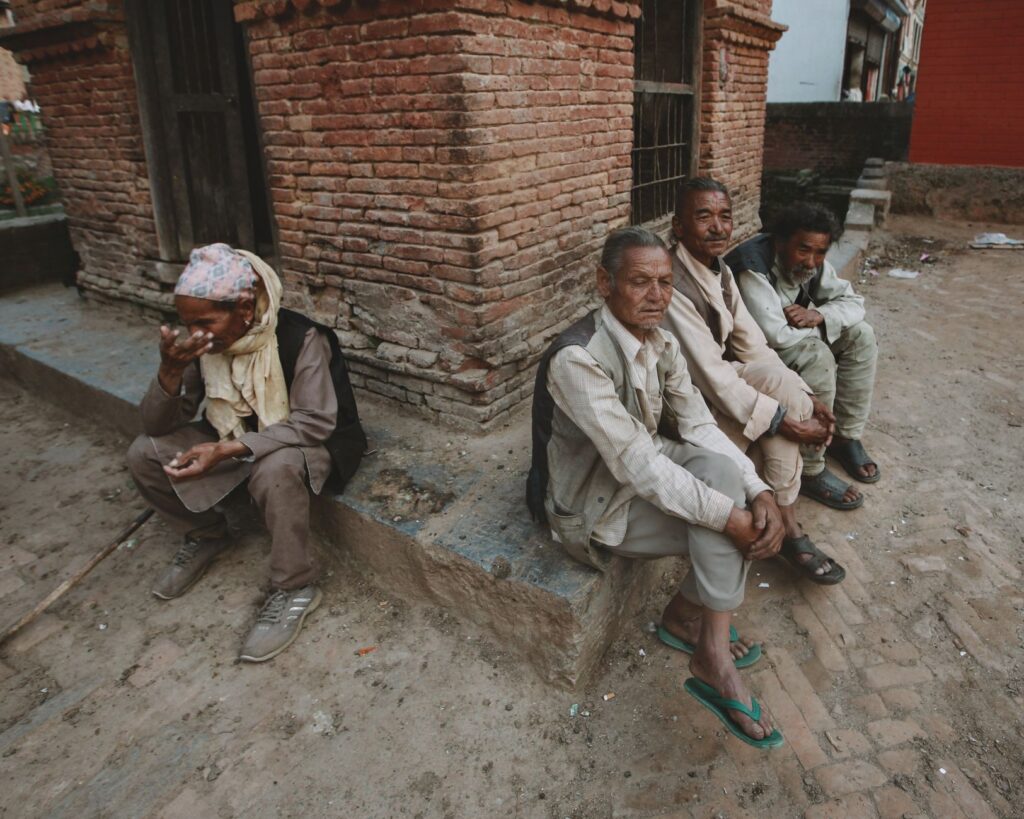 Elderly Nepali men sitting by a red brick wall in an urban setting, Kathmandu, Nepal.