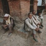 Elderly Nepali men sitting by a red brick wall in an urban setting, Kathmandu, Nepal.
