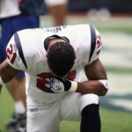 Football player in uniform kneeling before a game, displaying focus and determination.
