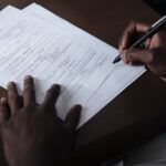 A detailed view of a man signing official documents with a pen at a table.